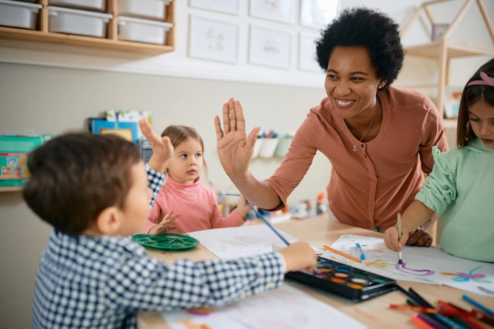 Happy teacher and small boy giving high-five during art class at kindergarten.